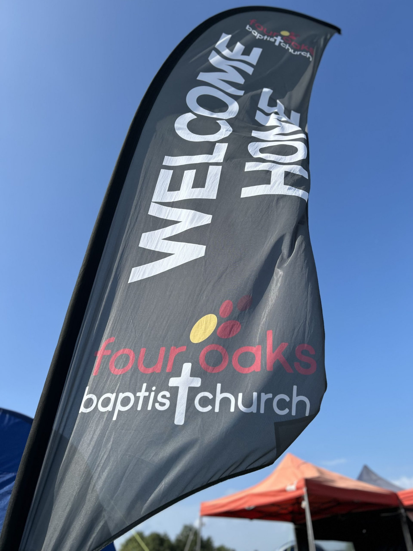 Four Oaks Baptist Church welcome flag against a blue sky