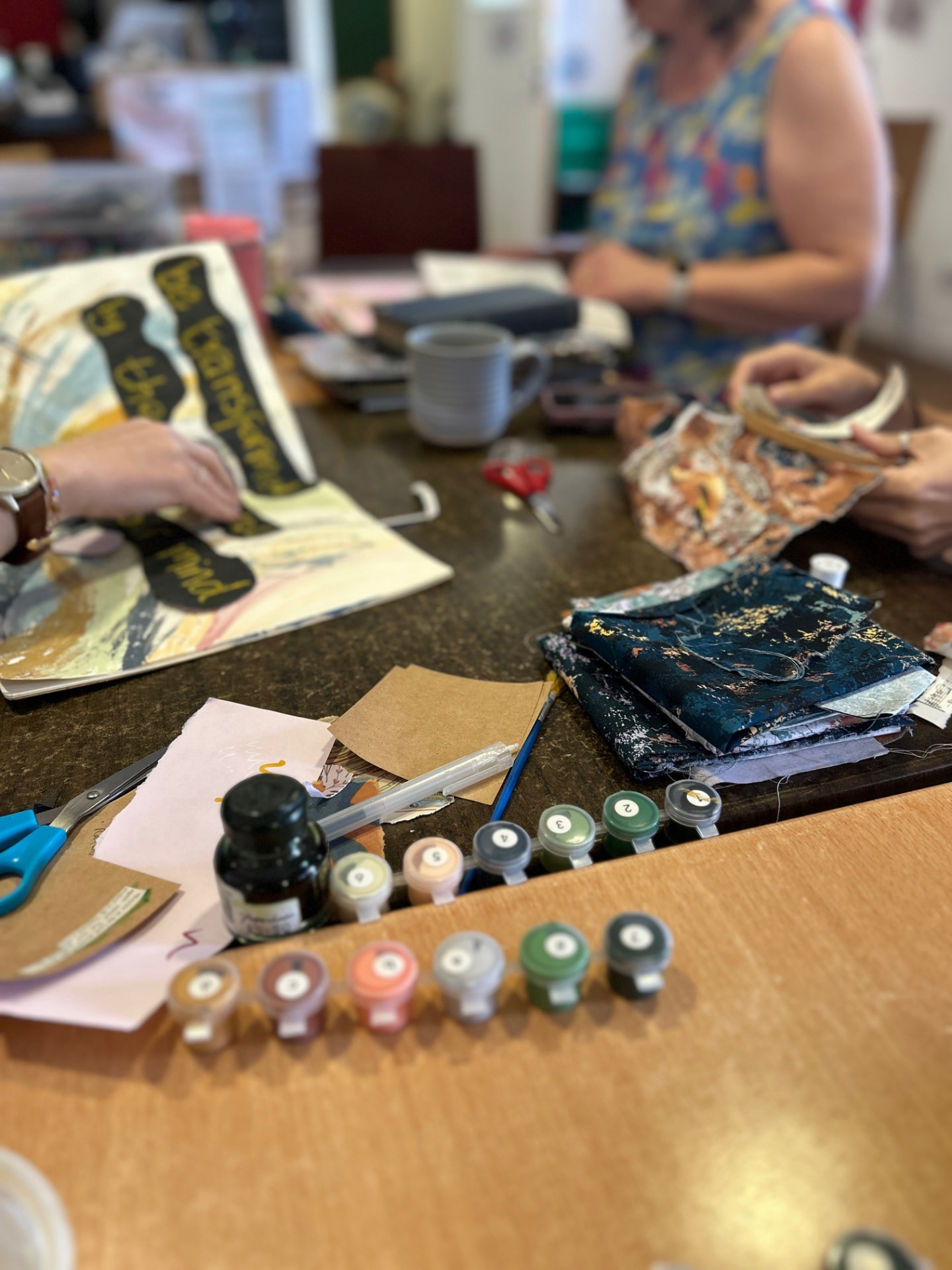 Craft table with paints, fabric and a hand-lettered journal page