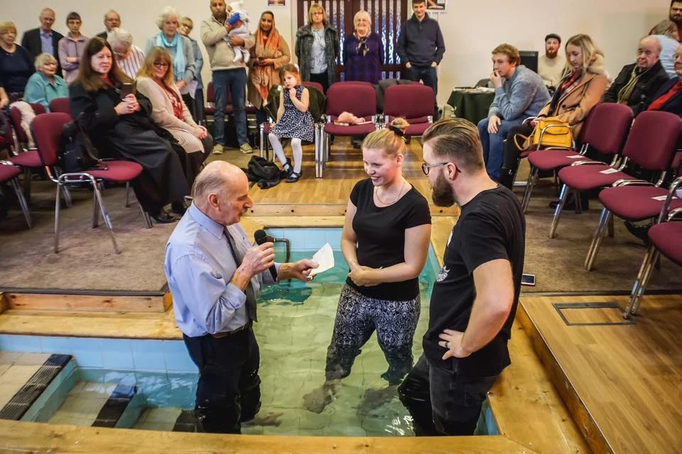 A believers' baptism by full immersion, with the congregation gathered around the baptistry
