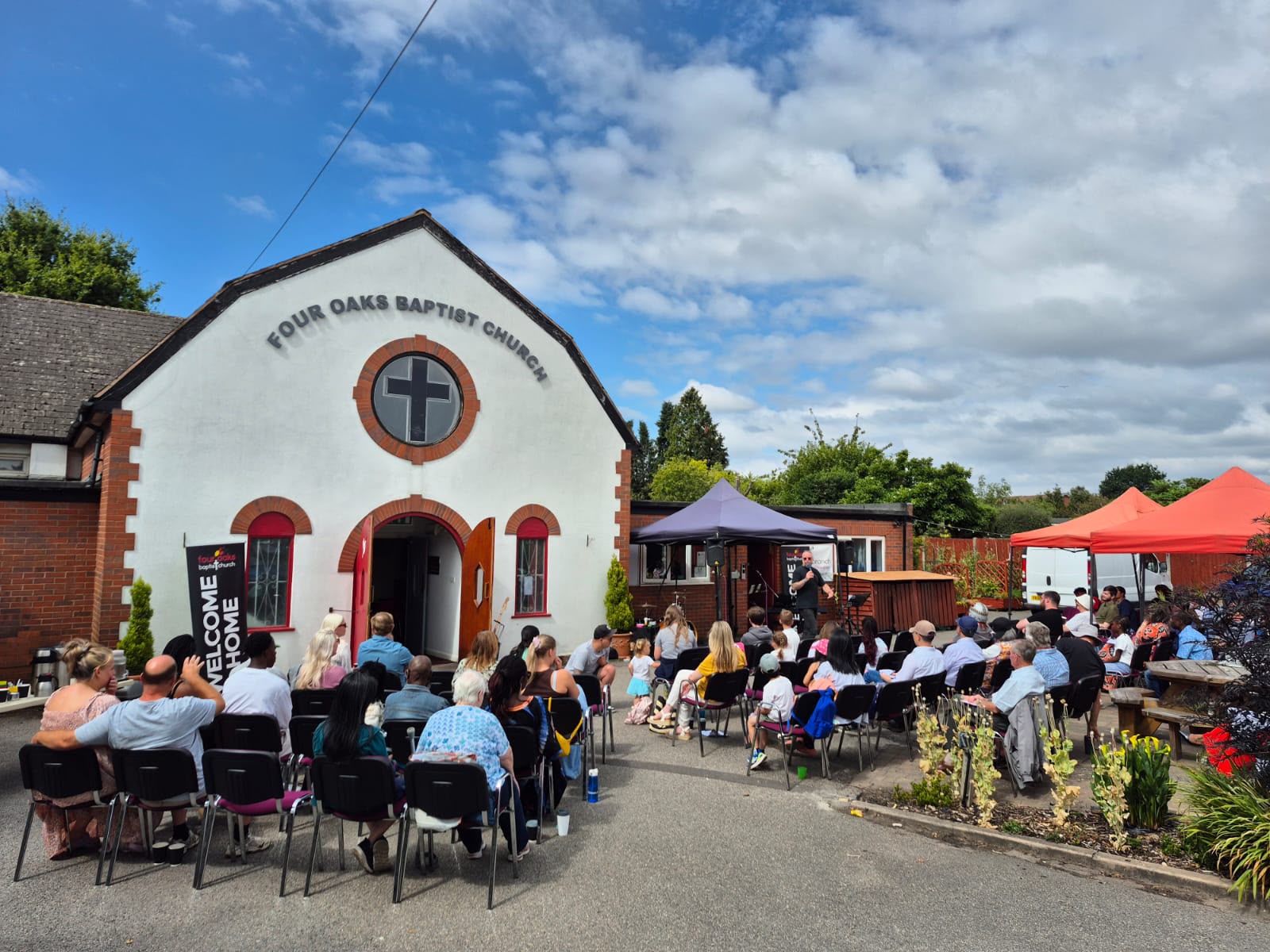 Congregation seated outdoors in front of Four Oaks Baptist Church on a sunny day