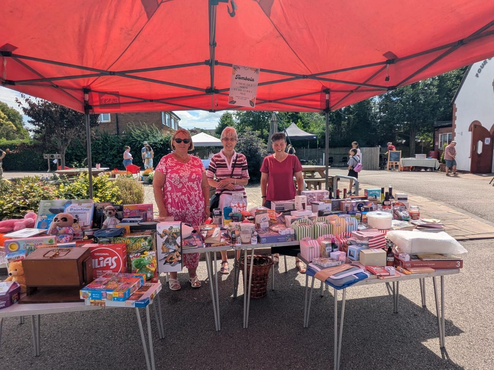 Three volunteers behind a tombola stall at the summer fete