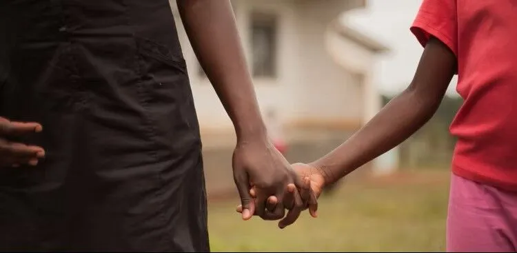 An adult and a child holding hands outside