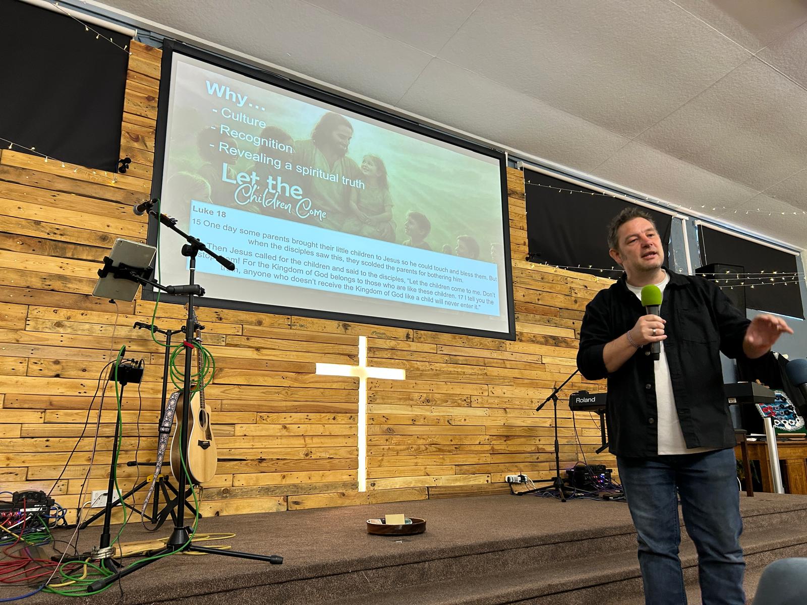 Andi from Kids UK preaching at Four Oaks Baptist Church in front of a Let the Children Come slide