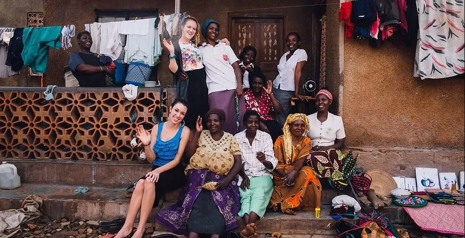 Kids Club Kampala volunteers and local women smiling together on the steps of a home in Kampala