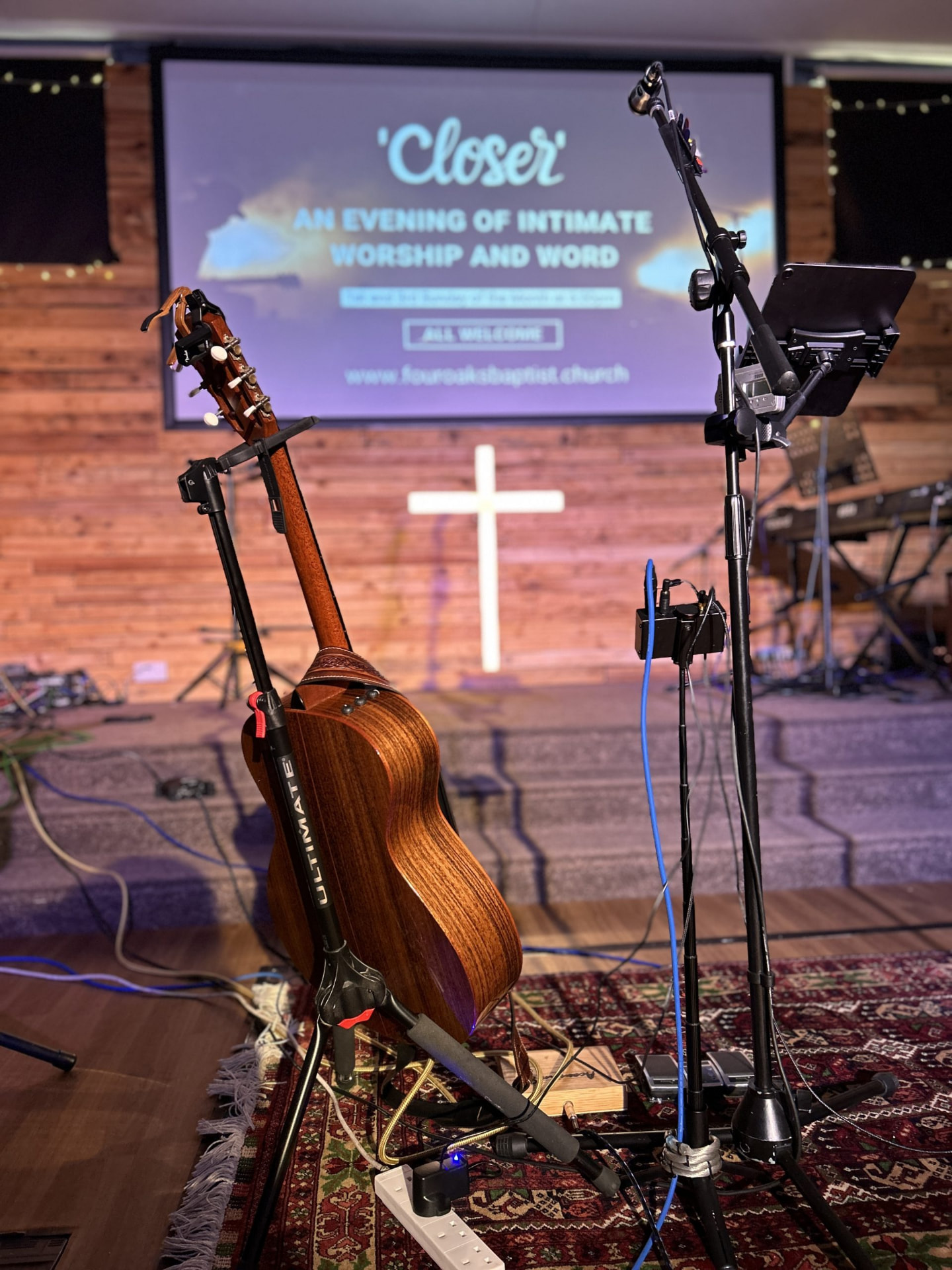 Guitar and microphone stands set up on the church stage with the Closer worship evening slide on screen