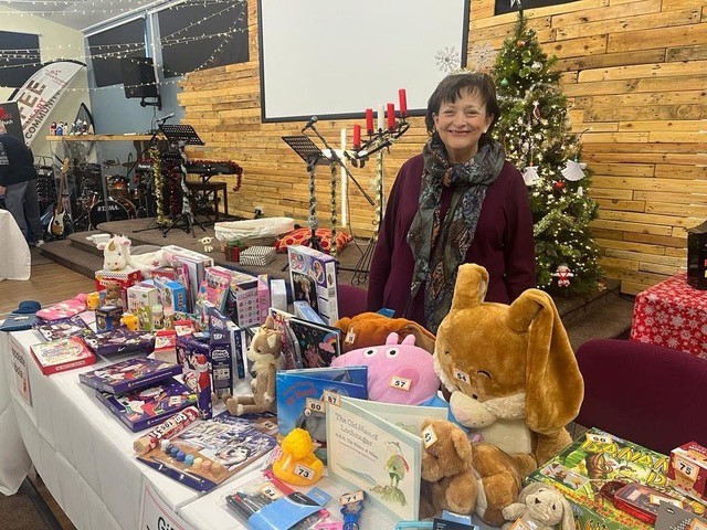 Volunteer standing behind a table of toys and gifts at the Christmas gift stall