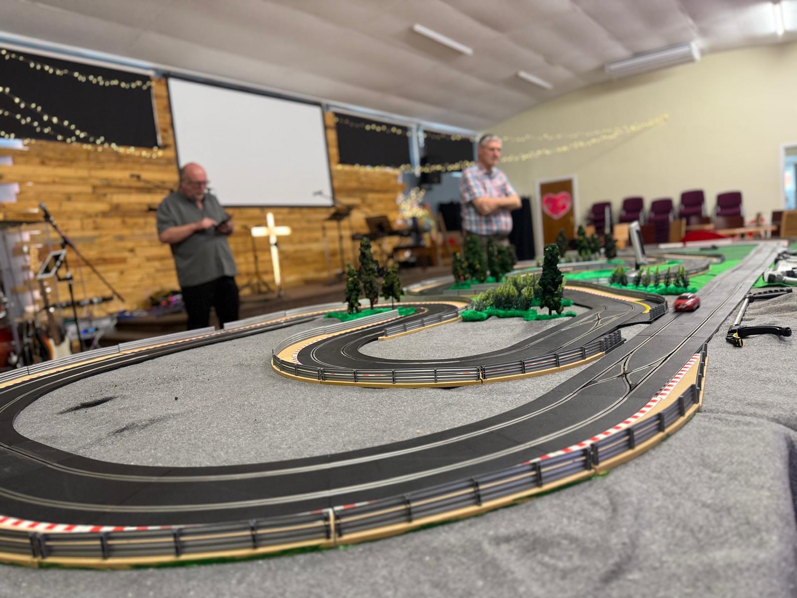 Large slot car racing track set up in the church with two men watching the race